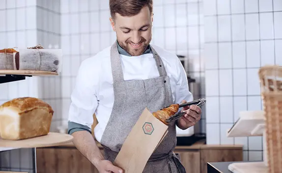 In einer Bäckerei verpackt ein Bäcker Backwaren in einem Faltenbeutel