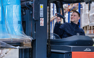 Ein Logistik-Mitarbeiter der PRODINGER Verpackung sitzt auf einem modernen Stapler und scannt eine Palette aus dem Hochregallager.