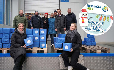 Mehrere PRODINGER Mitarbeiter stehen vor gepackten Paketen für die Weihnachtsspende.