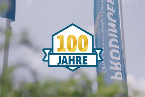 Videobotschaft von Steffen Prodinger - im Hintergrund wehen Fahnen von PRODINGER und im Vordergrund ist ein Icon zu 100 Jahren zu sehen.