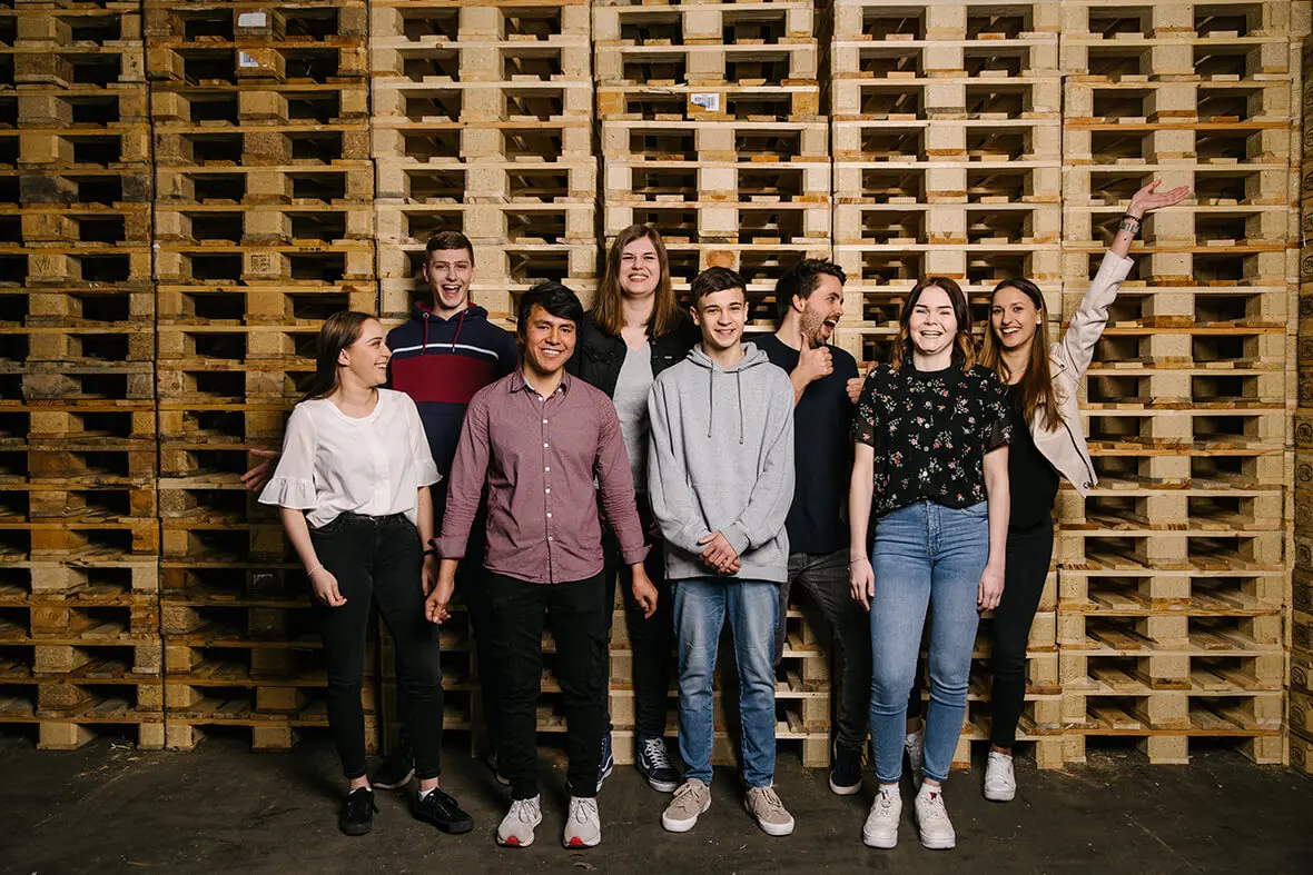 Einige Auszubildende von PRODINGER Verpackung stehen vor gestapelten Holz-Paletten.