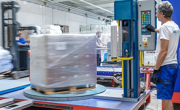 PRODINGER Mitarbeiter bedient Stretchmaschine in der Logistik, im Hintergrund steht weitere Verpackungstechnik