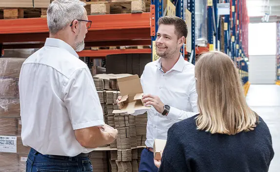 Beratungsgespräch vor einem Hochregallager in einem Logistikzentrum über die richtige Verpackungslösung für Kostensenkung und Prozessoptimierung rund um Transportverpackung