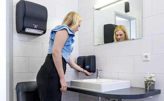 Eine Frau wäscht sich in einem modern ausgestatteten Waschraum mit Tubeless Spendersystem die Hände.